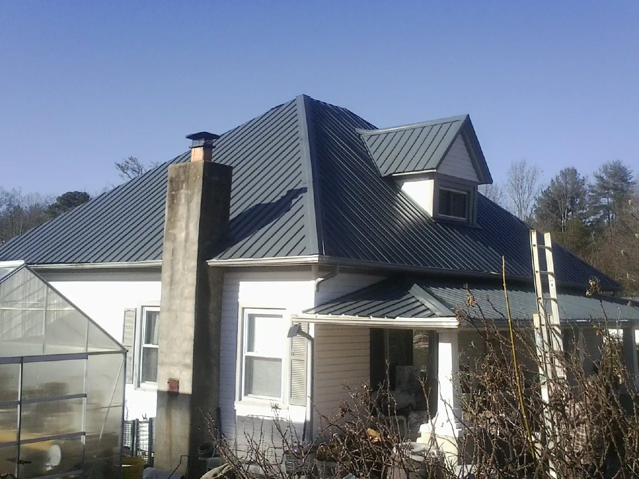 Dark blue standing seam metal roof on a white farmhouse with dormer — Slate & Tile Roof Repair by Roofing Brothers in Bennington